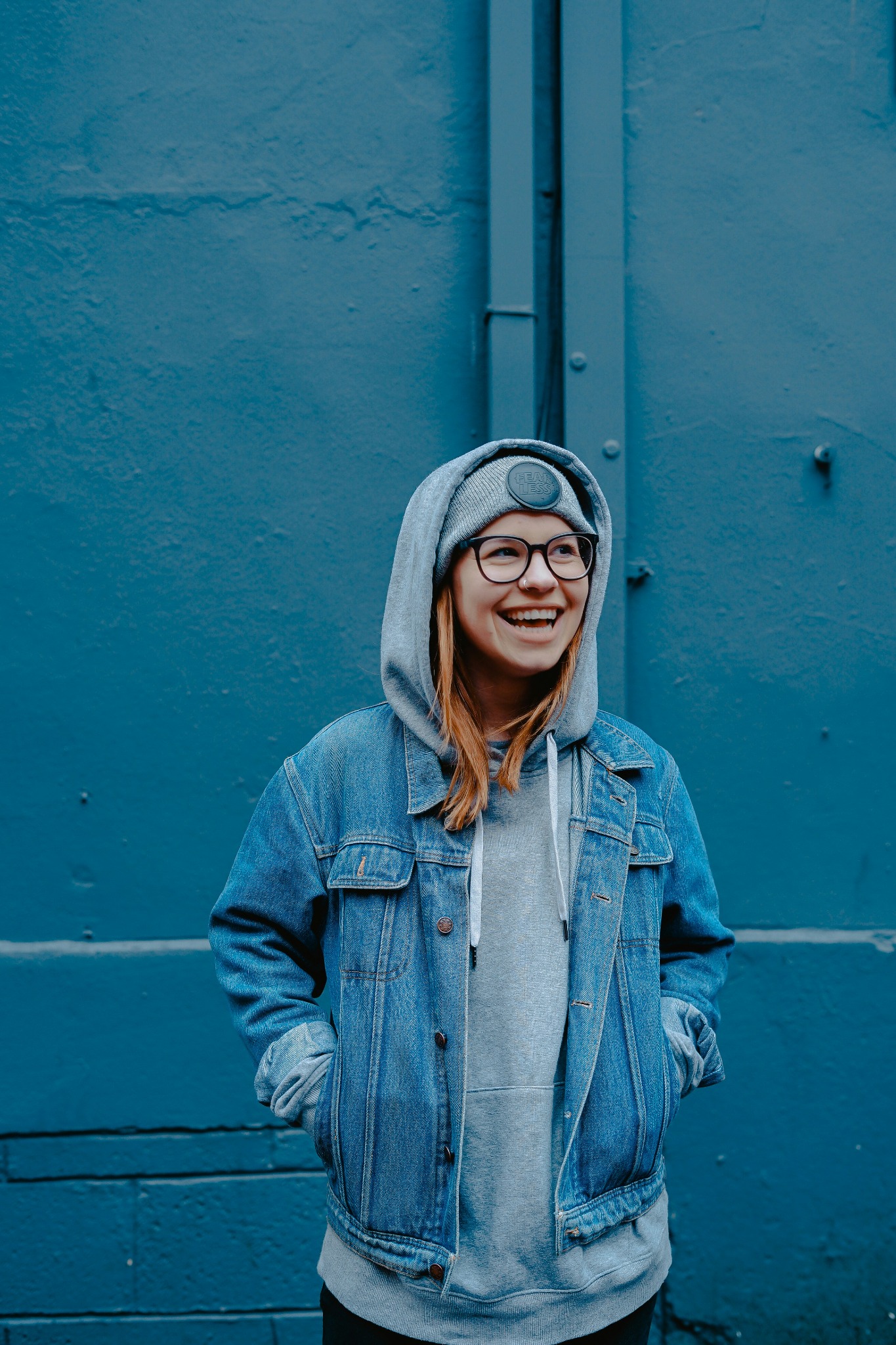 A woman laughing in a denim jacket against a blue wall